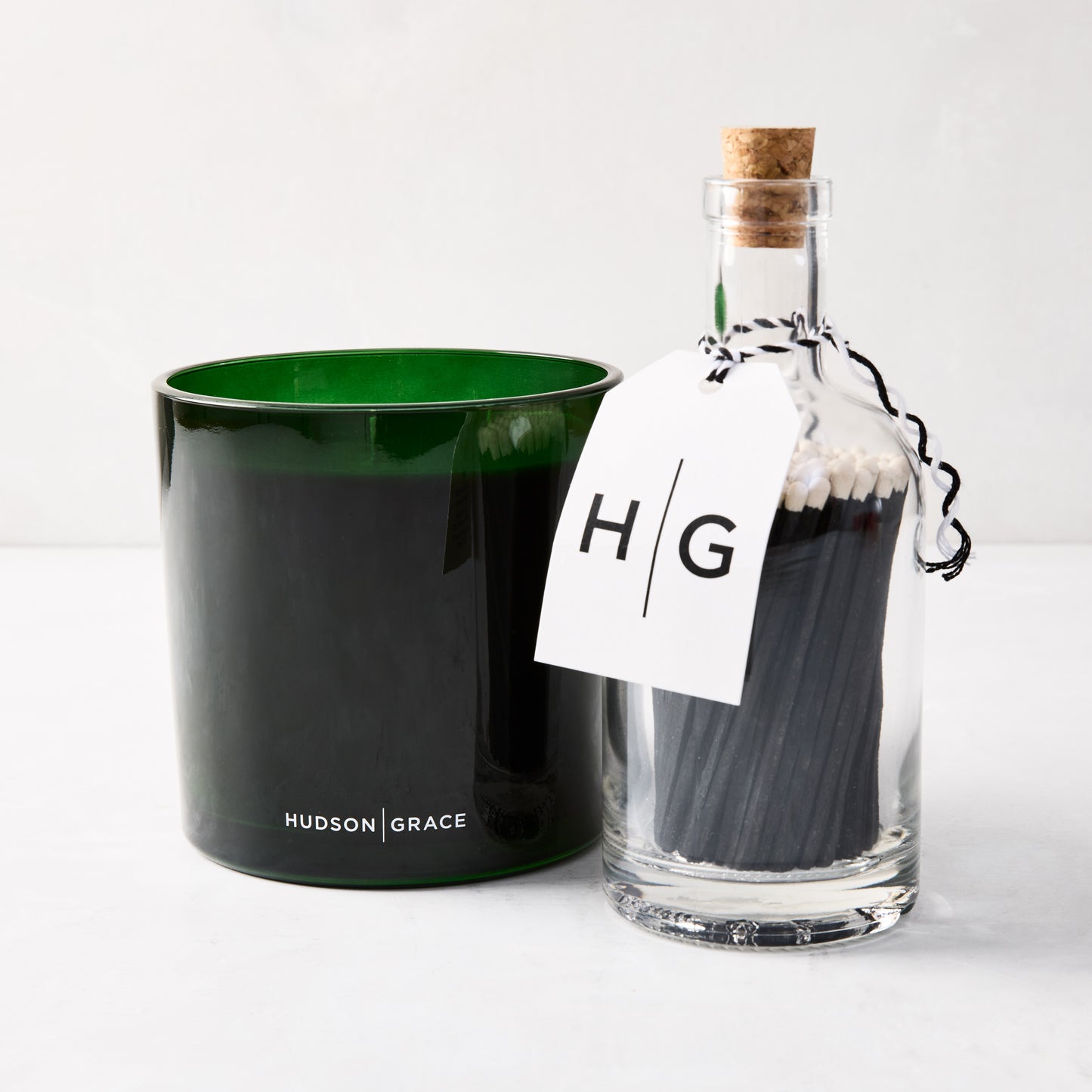 Green glass 3-wick candle and clear glass bottle with black matches and "HG" tag.