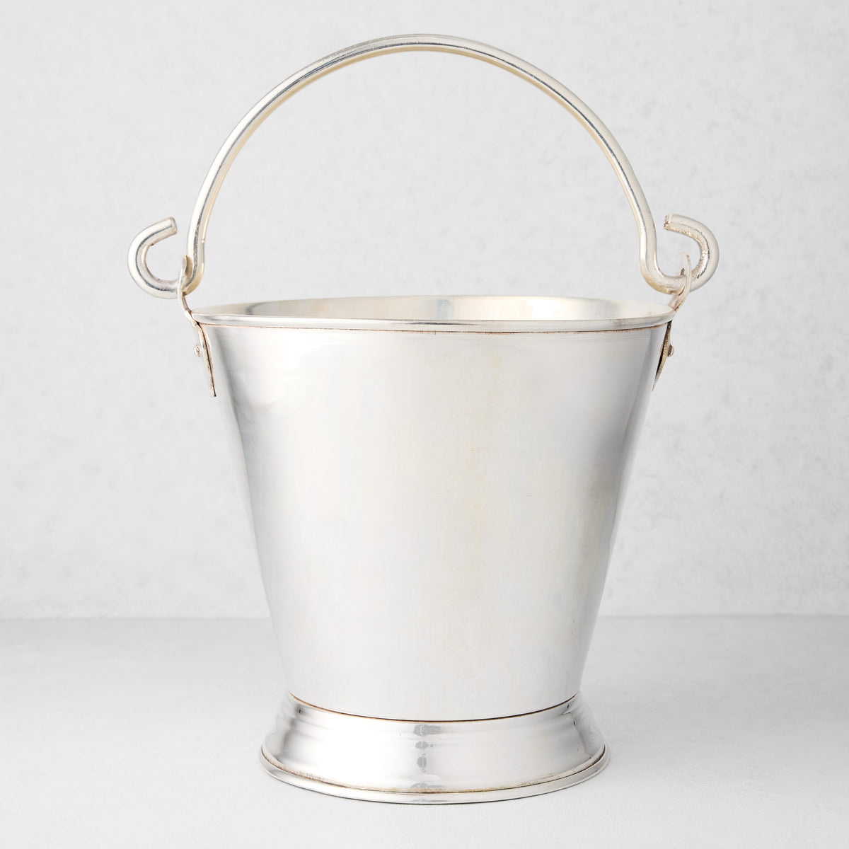 Vintage silverplate champagne bucket with a tapered body, pedestal base, and arched swing handle on a white background.