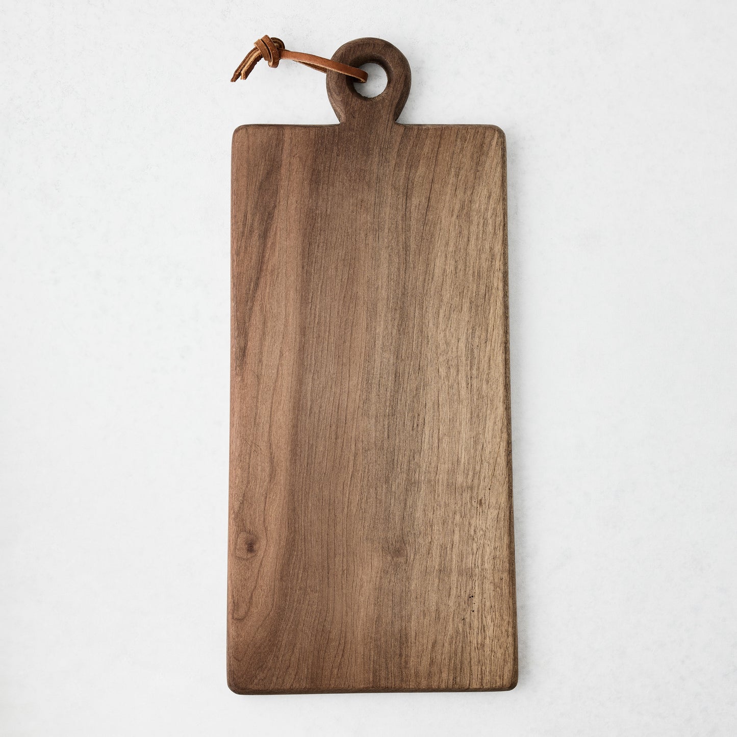 Artisan rectangular walnut wood serve board with a round handle and brown leather cord.