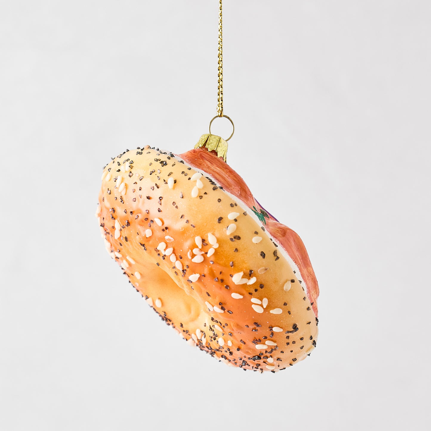Hand-painted glass and resin bagel and lox Christmas ornament with sesame seeds and glitter accents.
