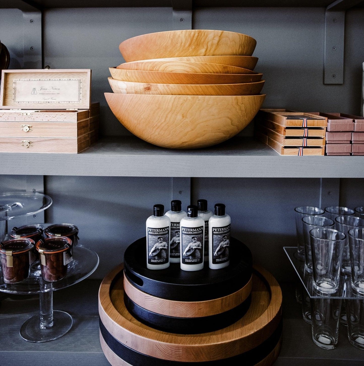 Peterman's Beeswax Conditioner bottles on a black stand, with wooden bowls and other products on shelves.