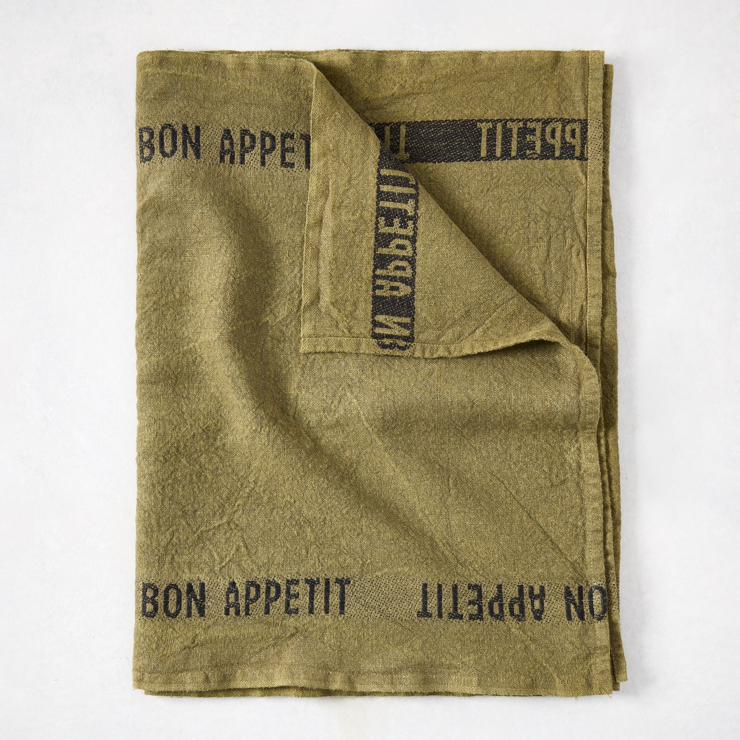 Folded green linen table runner with "BON APPETIT" in black text.