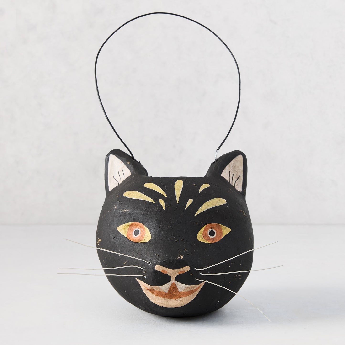 Distressed black papier-mâché cat candy bucket with gold accents, white whiskers, and a wire handle.