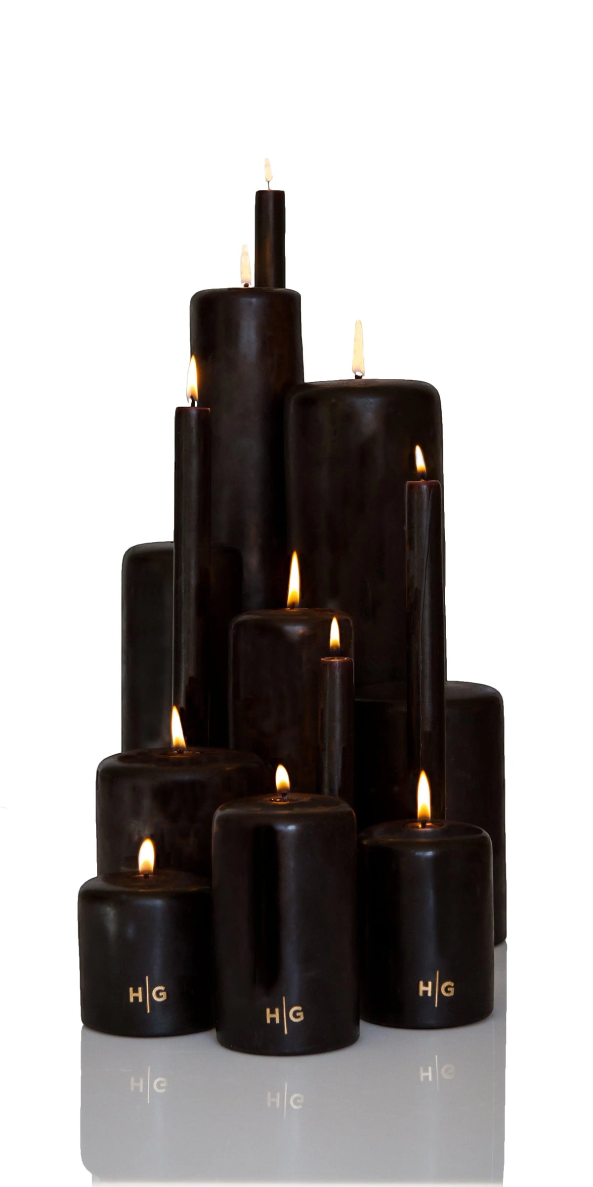 HG Black unscented pillar candles, various sizes, with gold HG logo and lit wicks.