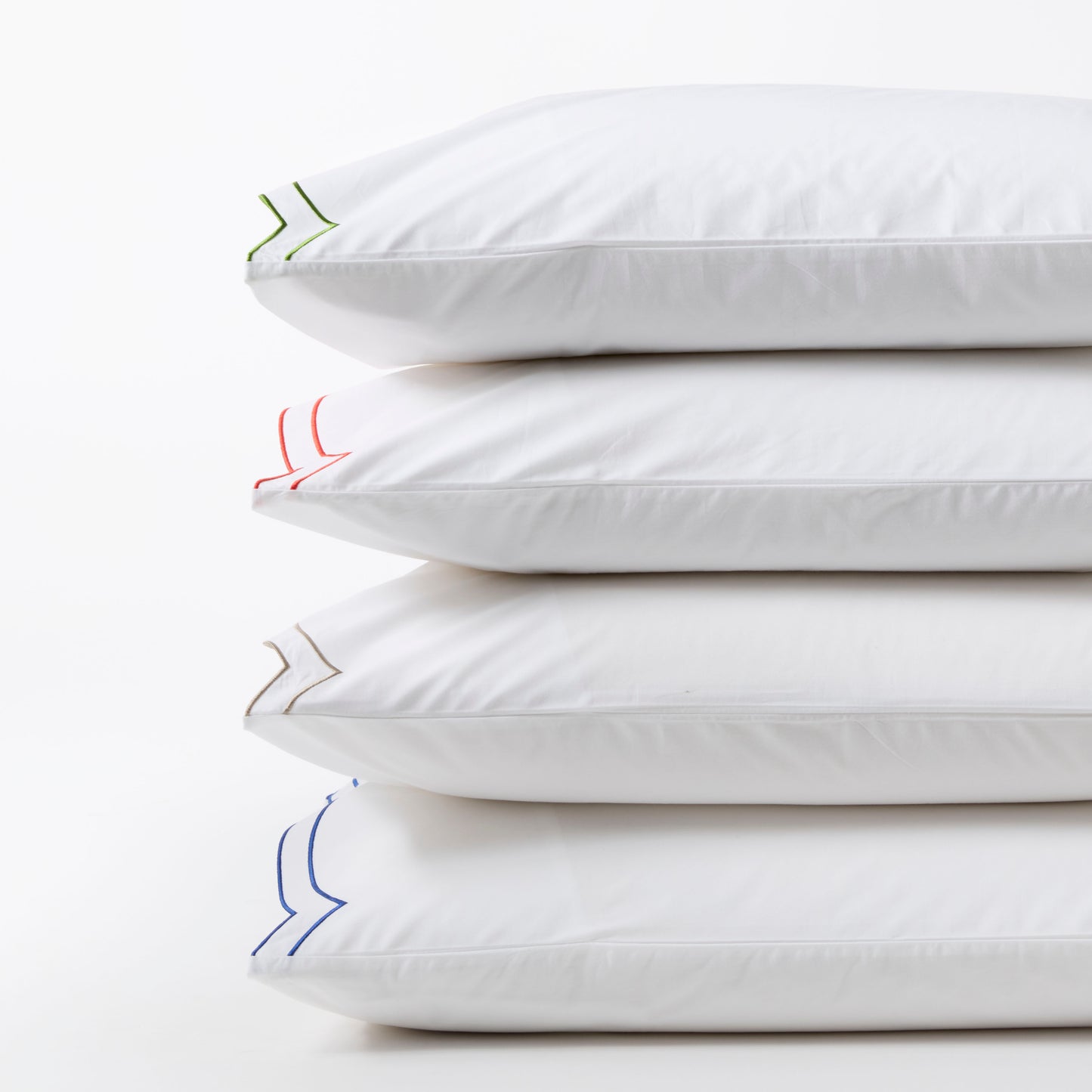 Stack of four white organic cotton percale pillow shams with double scallop stitch embroidery in blue, tan, red, and green.