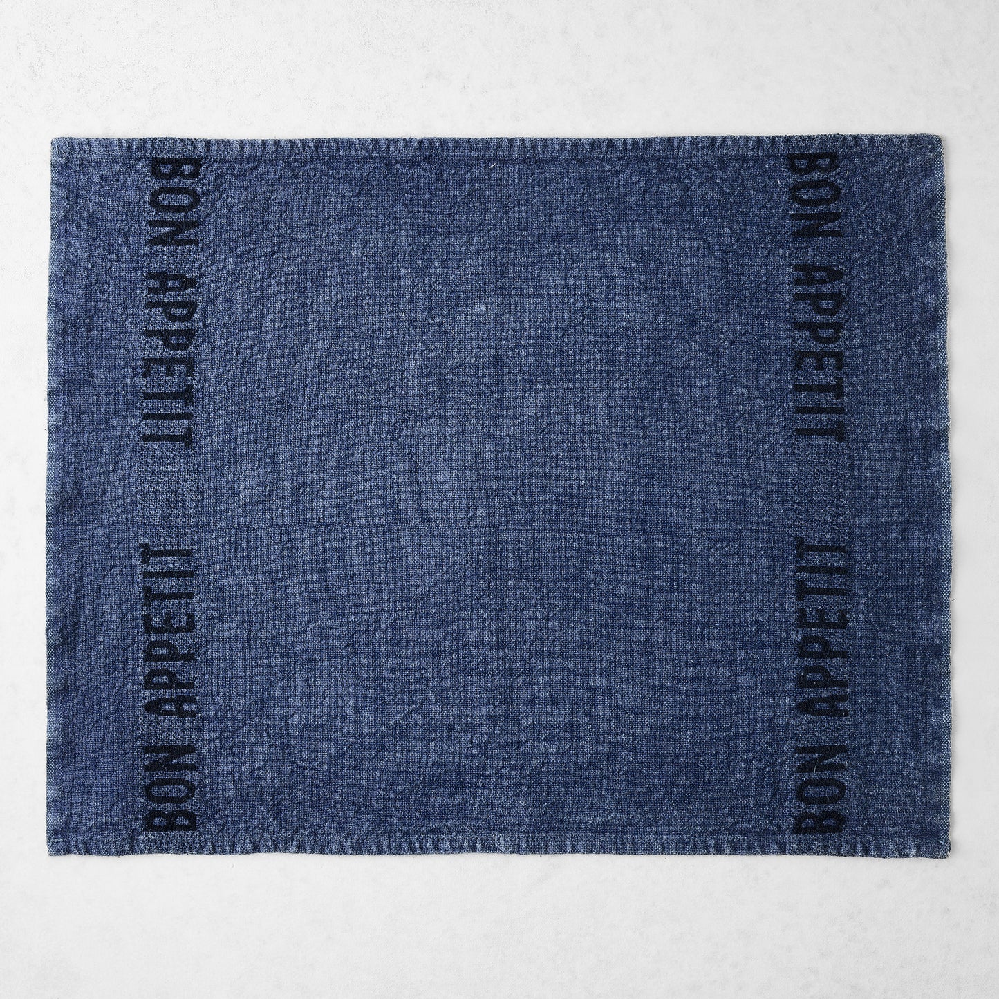 Indigo blue linen napkin with "BON APPETIT" in black lettering on two sides.