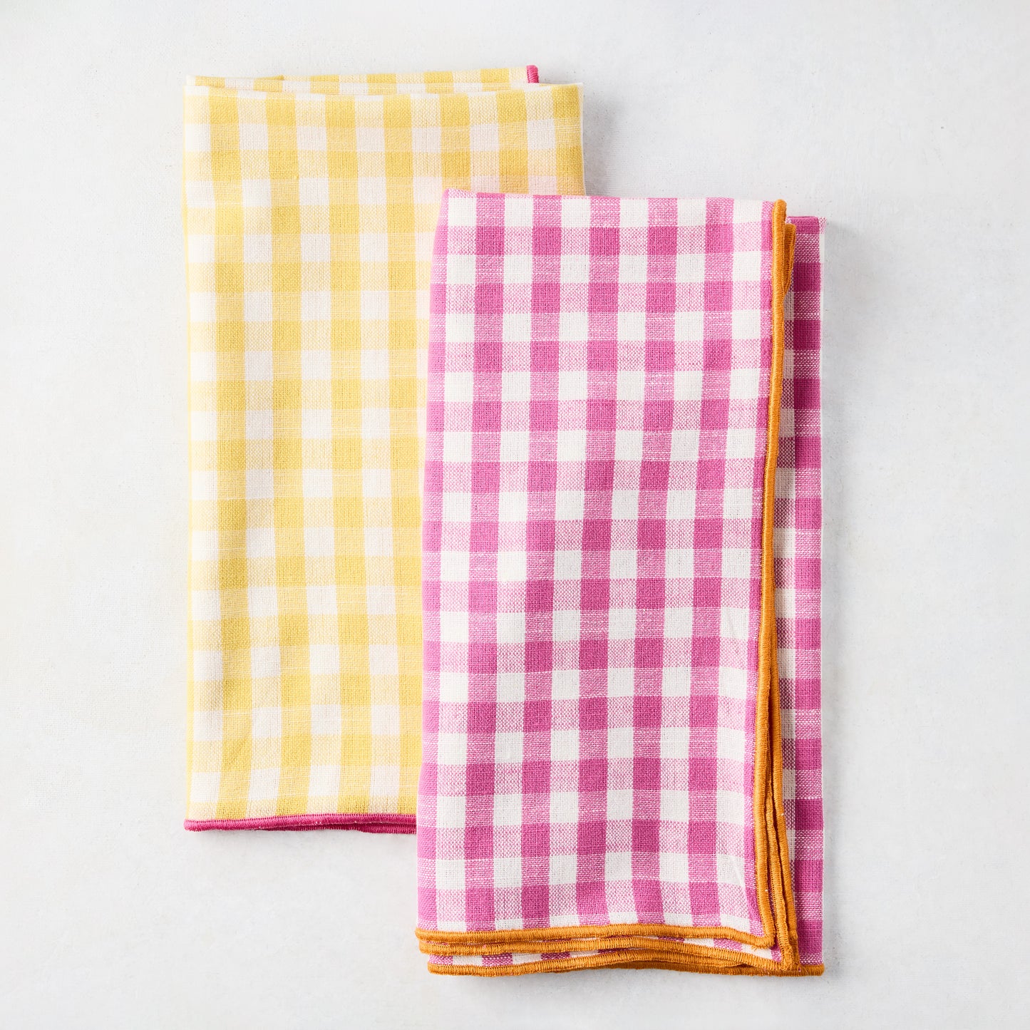 Chatham Yellow Gingham Cotton Napkin with Pink Trim, folded, next to a pink gingham napkin.