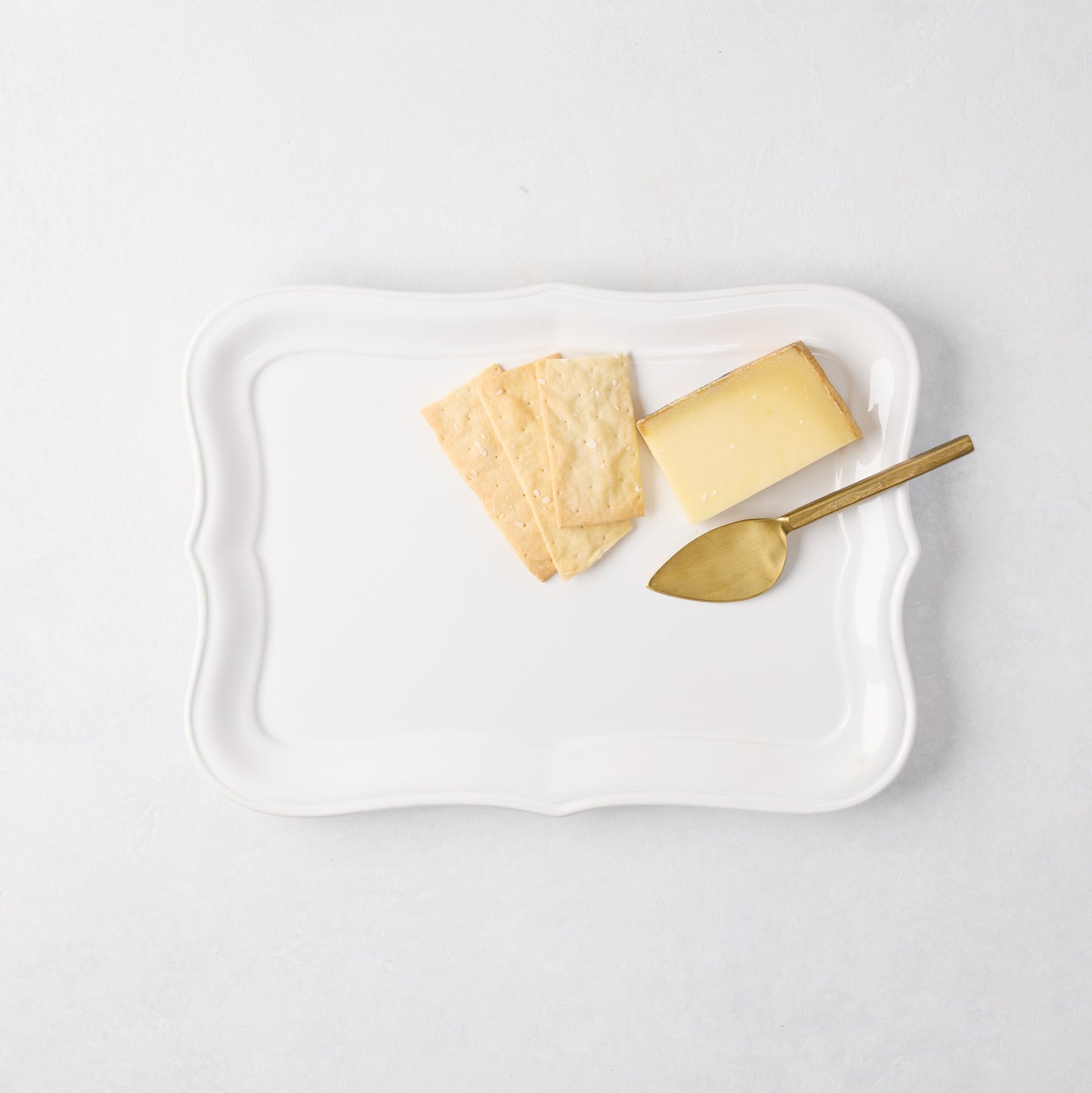 White Colette Small Ceramic Serving Platter with scalloped edges, holding crackers, cheese, and a gold server.