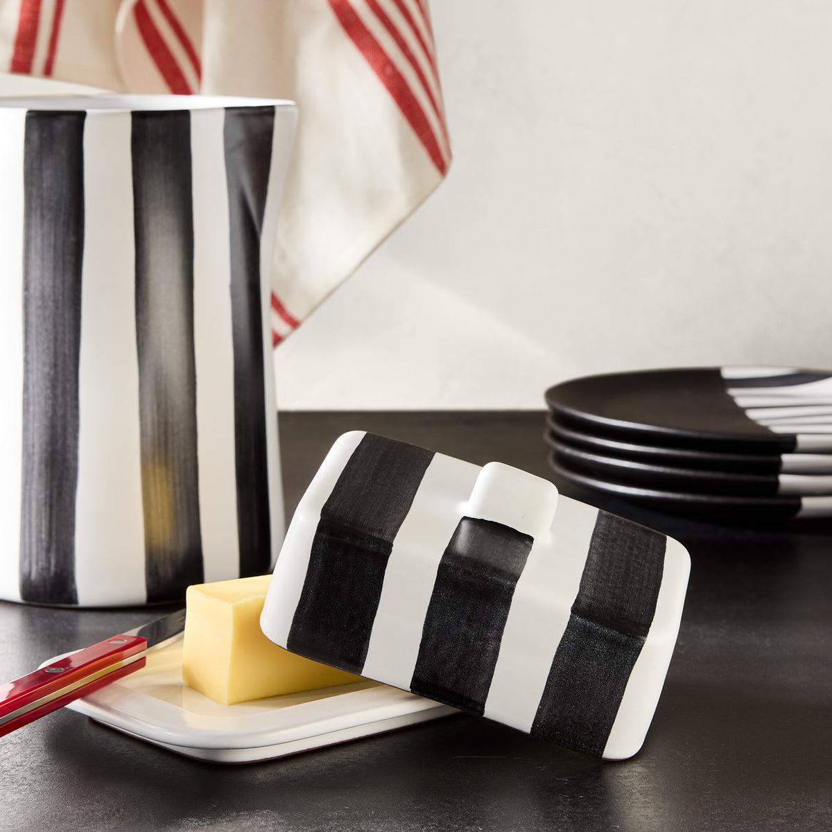 Diane Keaton + Hudson Grace black and white striped ceramic butter dish and pitcher on a dark surface.