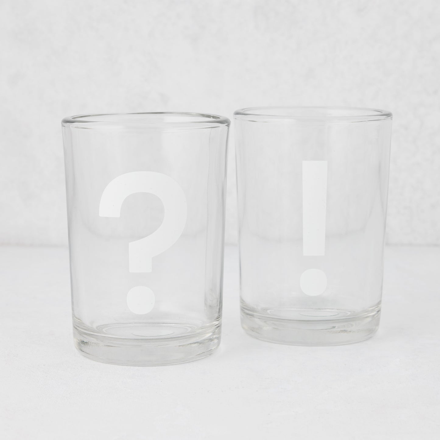 Two clear glass tumblers, one with a white question mark, one with a white exclamation point.