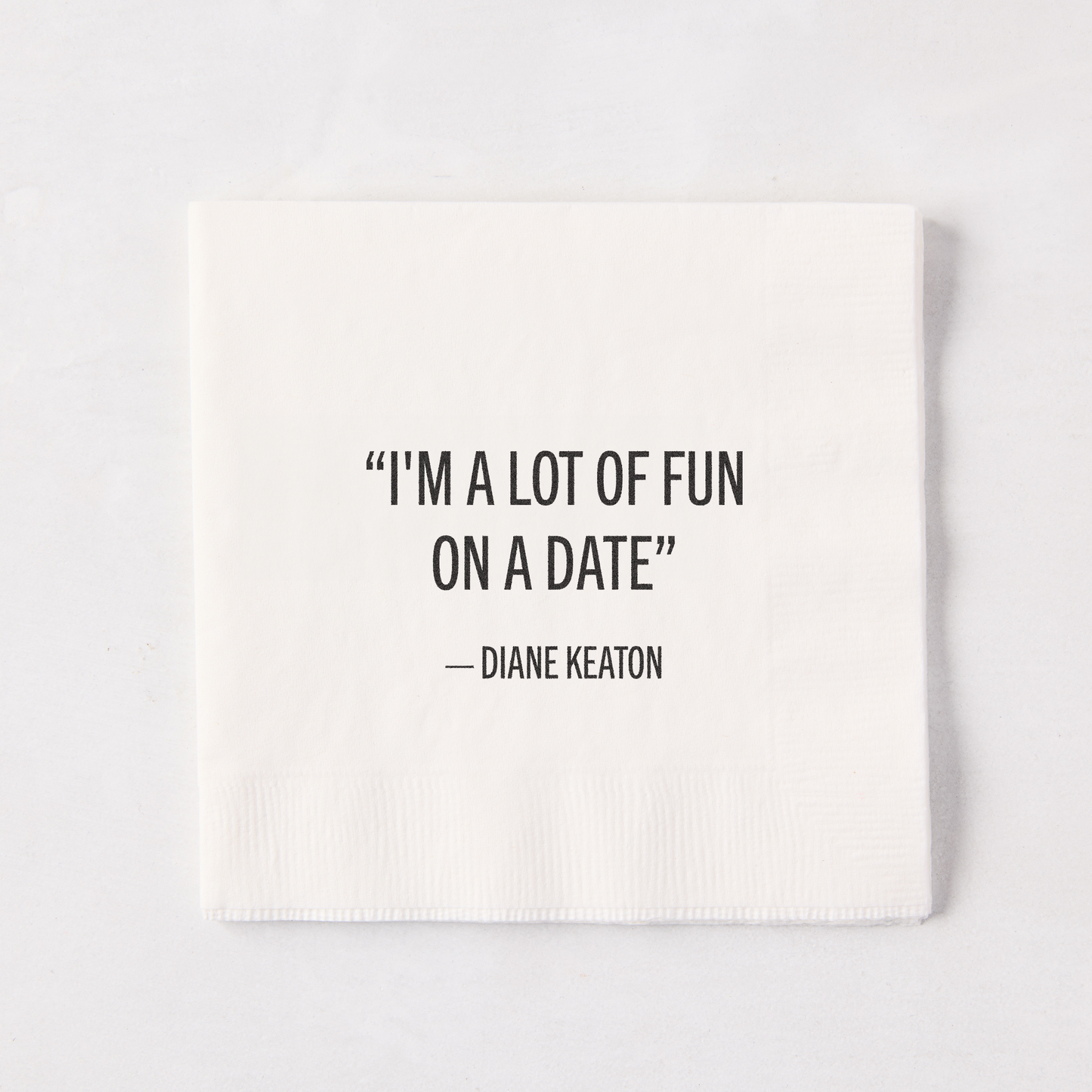White 5.5" square paper cocktail napkin with "I'M A LOT OF FUN ON A DATE" - DIANE KEATON quote.