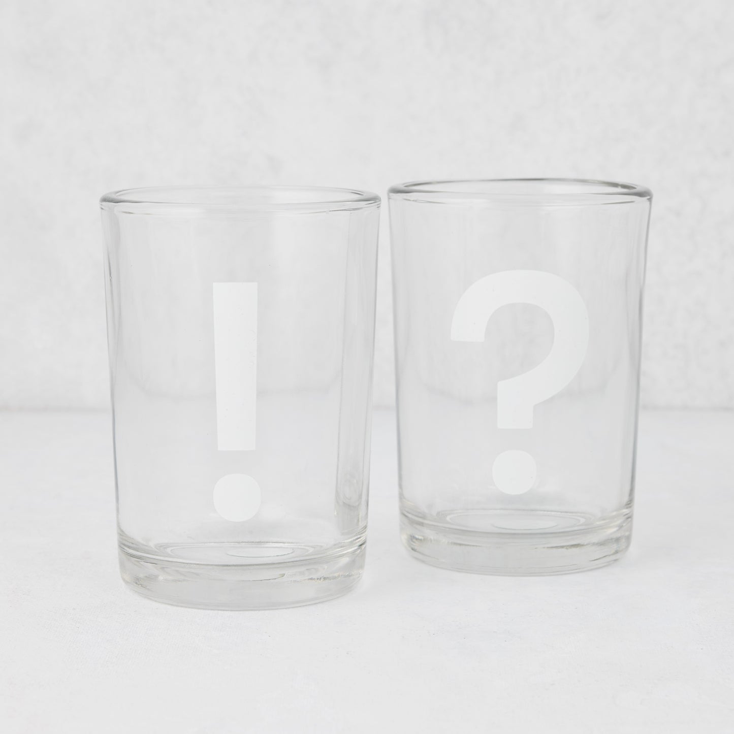 Two clear glass tumblers, one with a white exclamation mark, the other with a white question mark.