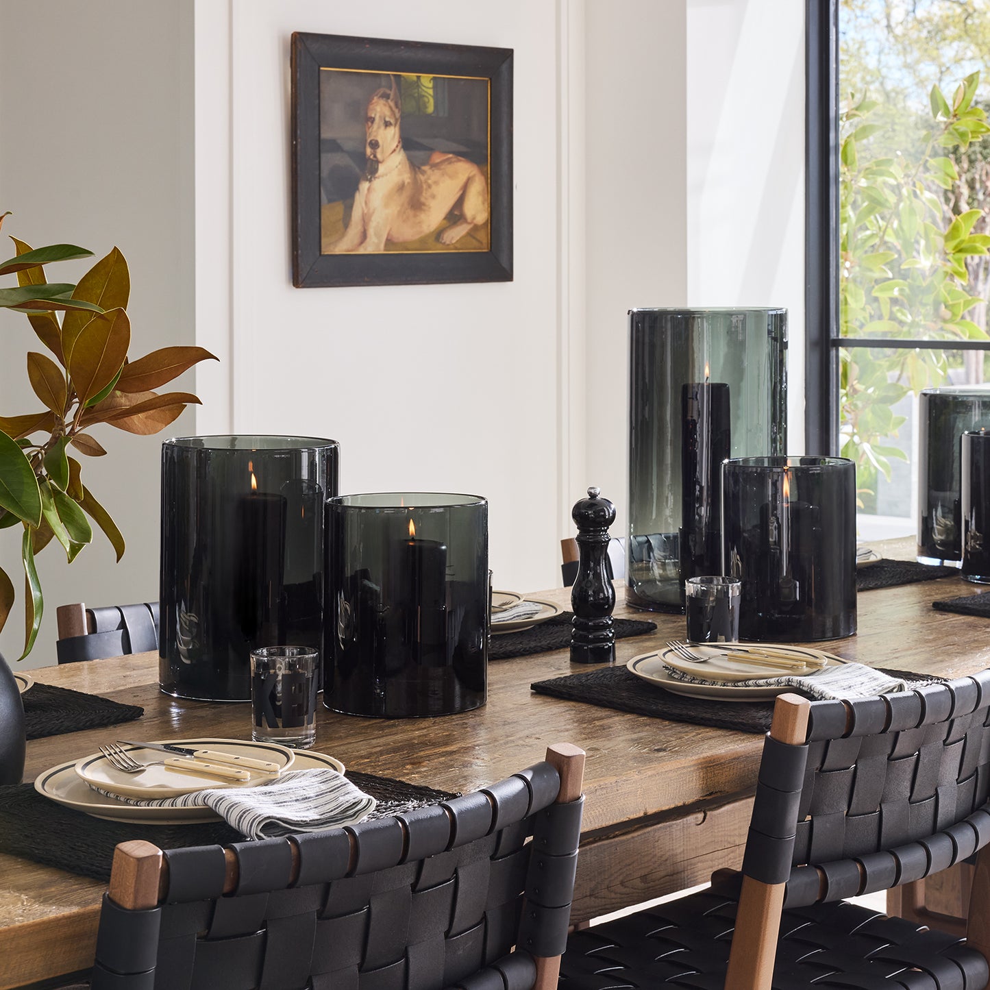 Diane Keaton + Hudson Grace large smoke grey glass hurricanes with pillar candles on a wooden dining table.