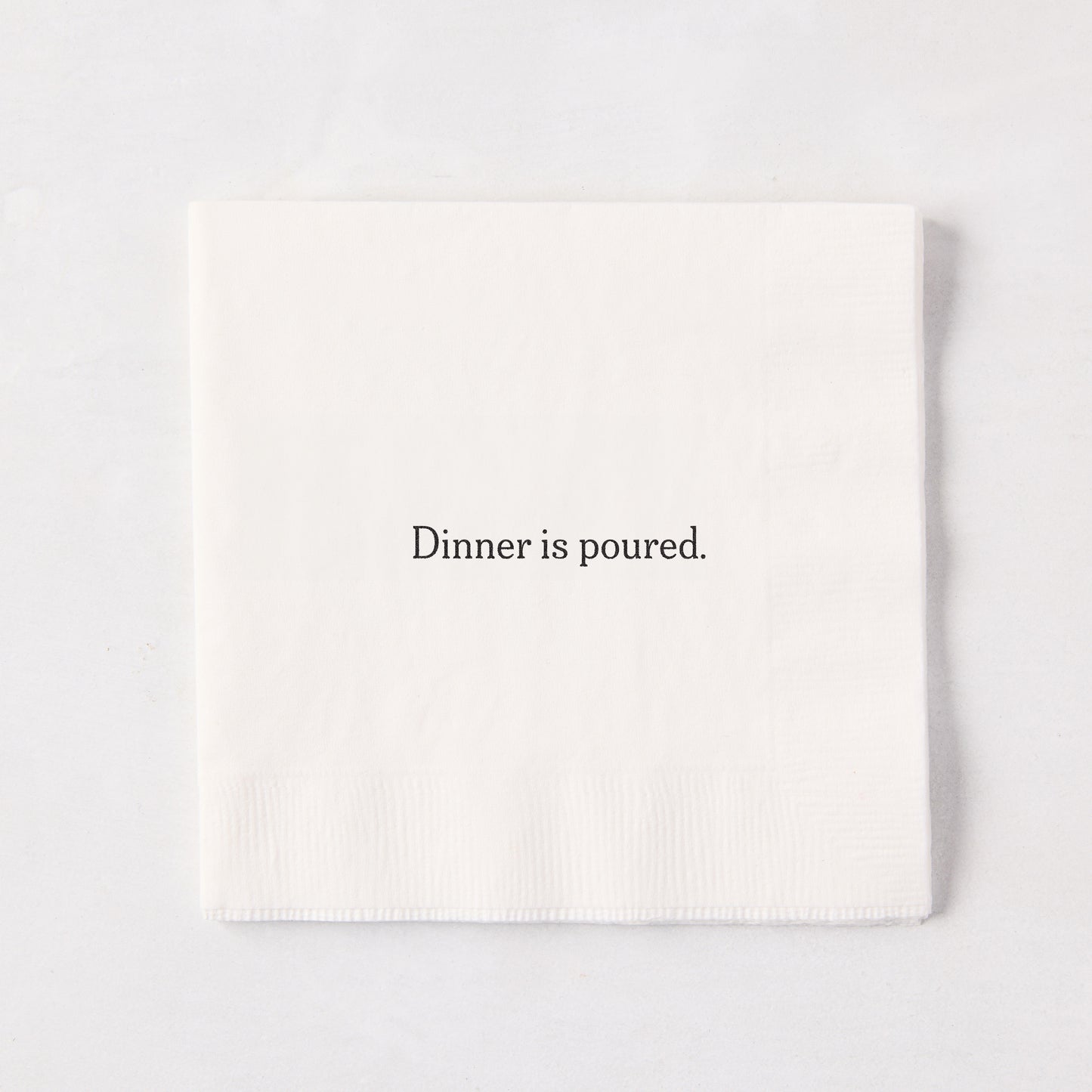 White 5.5" square paper cocktail napkin with "Dinner is poured." in black text.