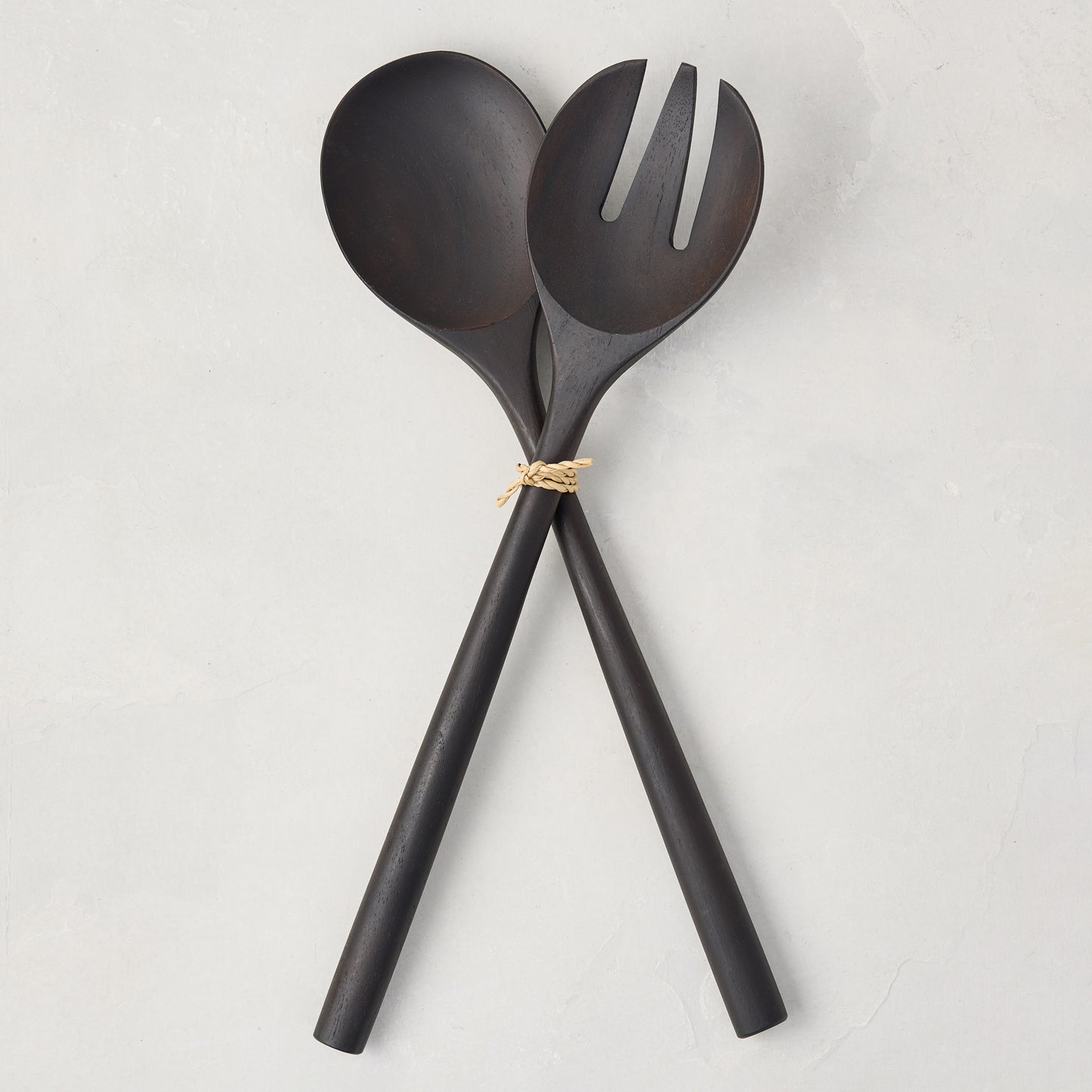 Ebony teak wood long-handled 2-piece serving set, spoon and fork, tied with twine on a white background.