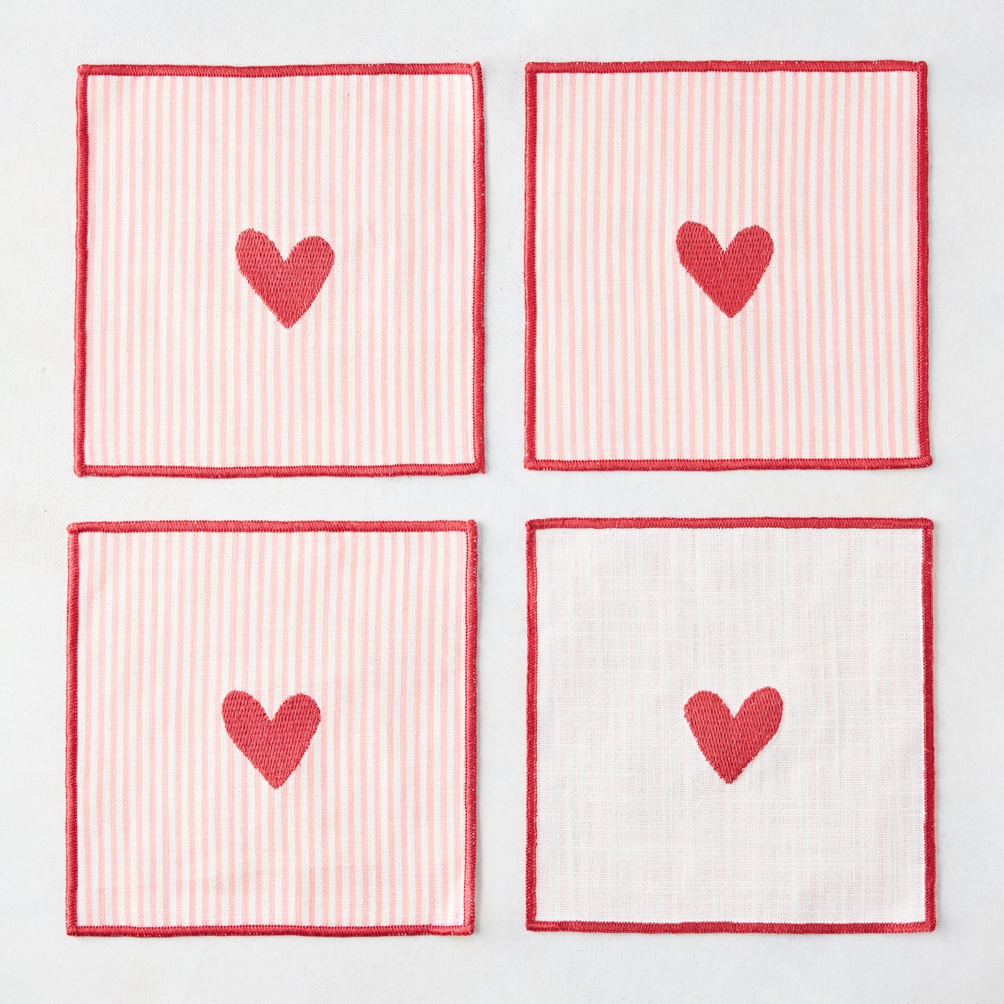 Set of 4 cotton coasters with red embroidered hearts, red edges, and pale pink and white stripes.