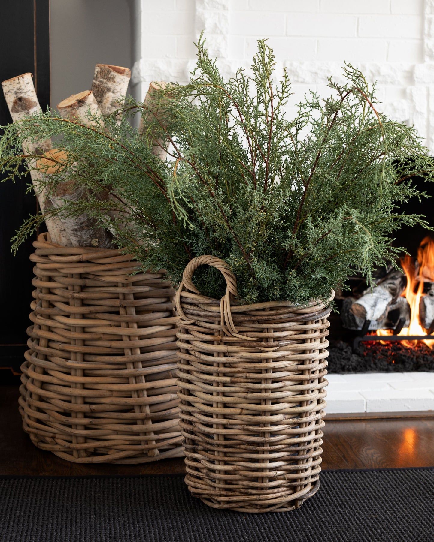 Fresh Carolina Sapphire greenery stems in a tall woven wicker basket next to a fireplace.