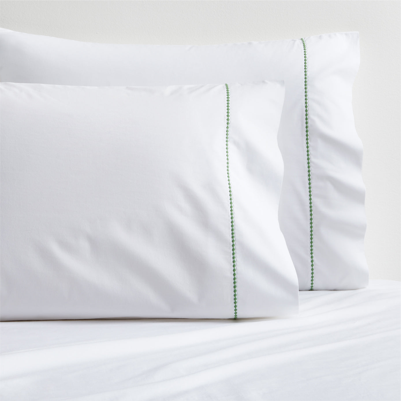 Set of 2 white percale pillowcases with a green diamond embroidered border.