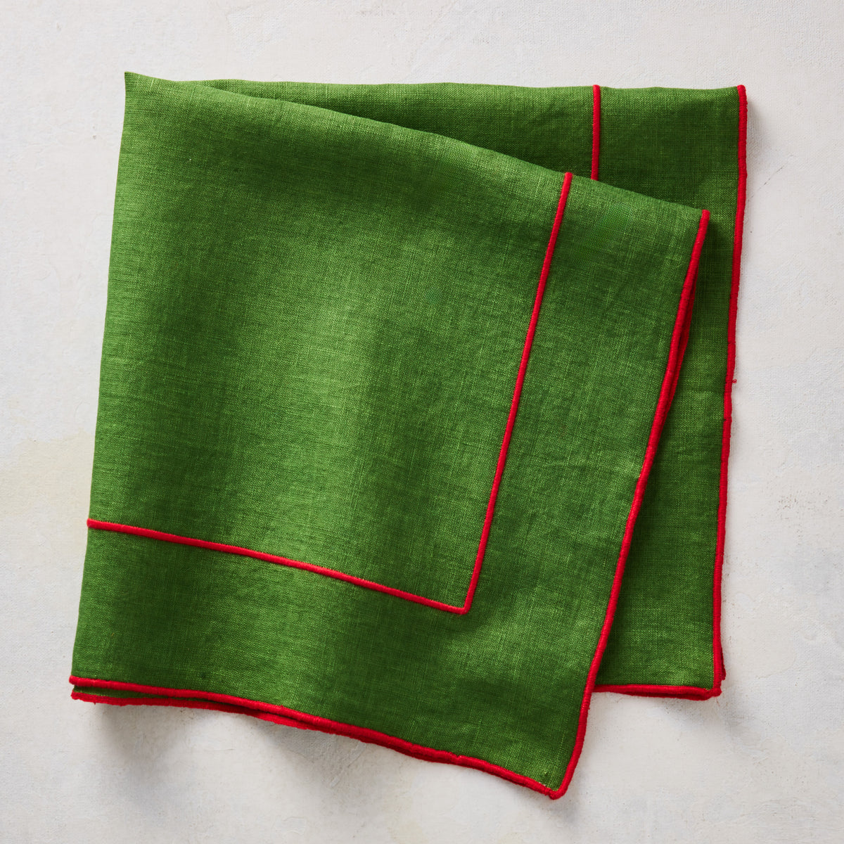 Green linen napkin with red embroidered border detail, folded on a light textured surface.
