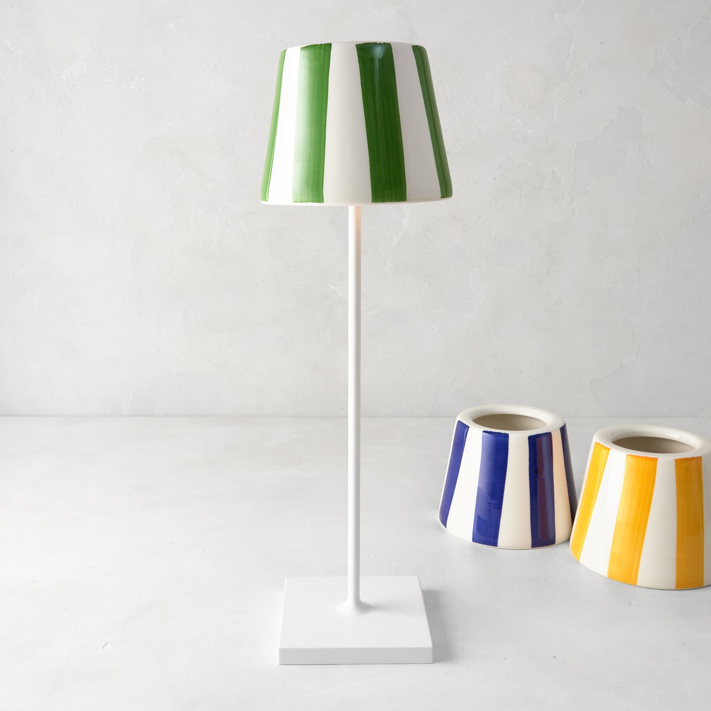 Green and white striped ceramic lamp shade on a white lamp, with blue and yellow striped shades nearby.