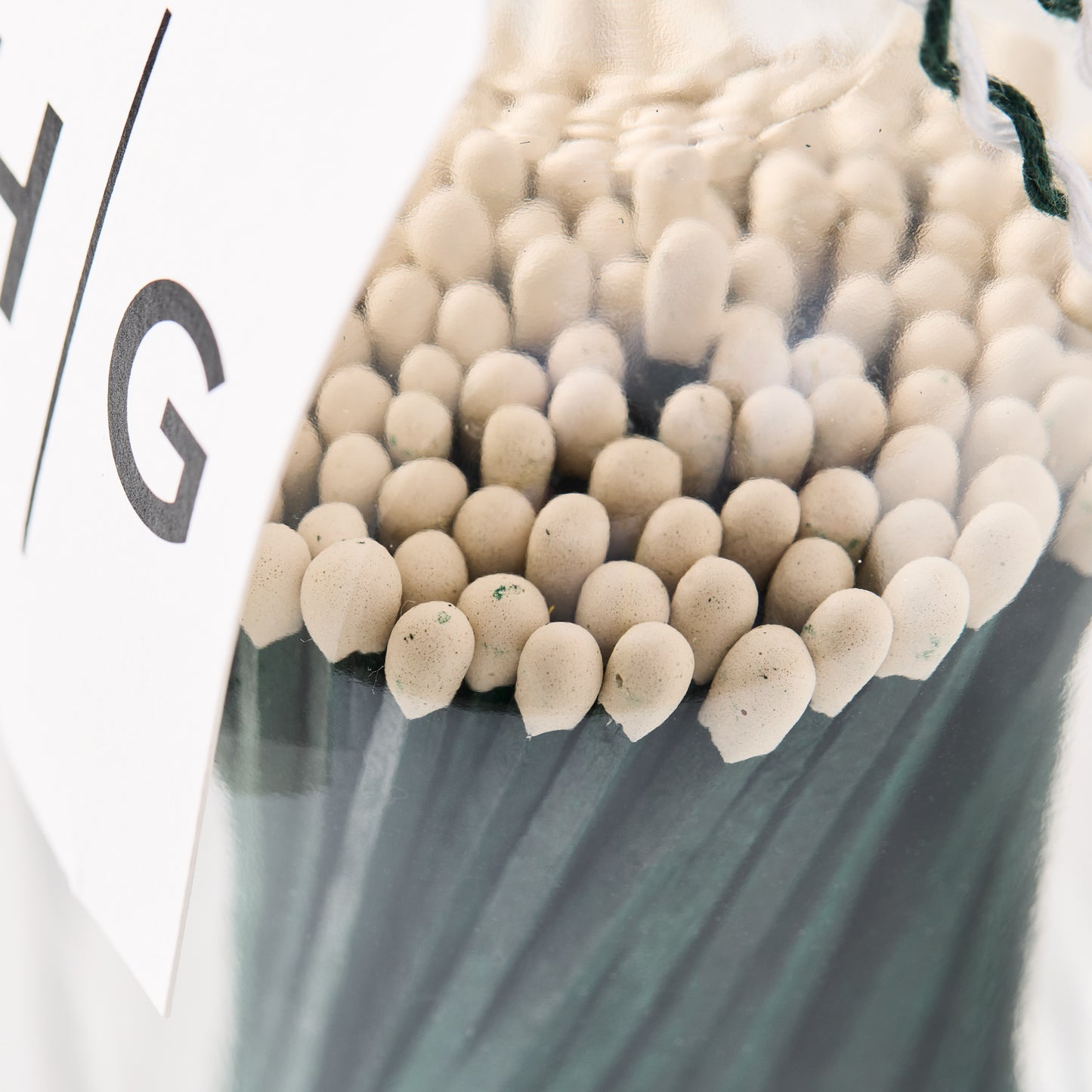 Oversized green matches with white tips in a clear glass bottle, cork topper, and white label.