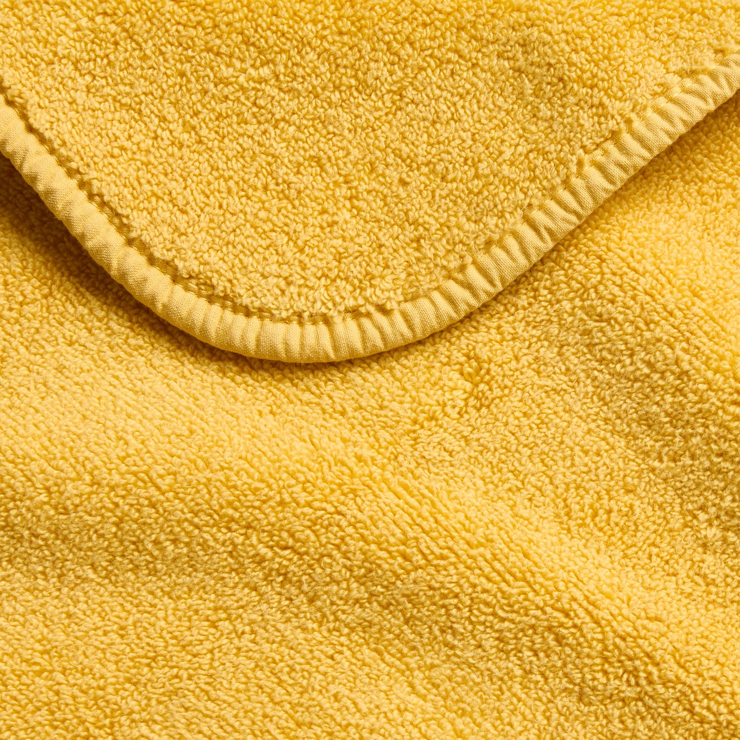 Bright yellow Signature washcloth made of soft, absorbent cotton terry fabric with a stitched hemmed edge.
