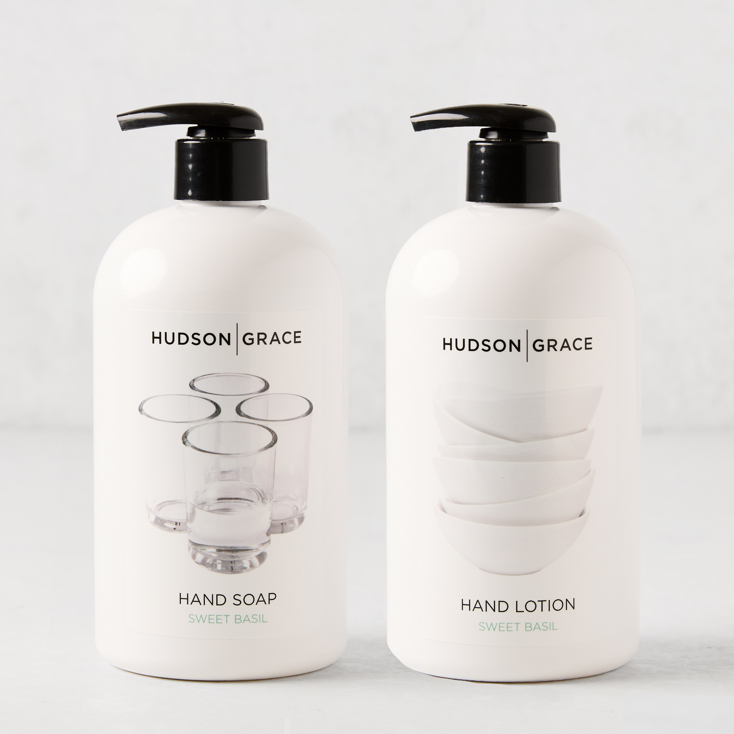 Two white Hudson Grace Sweet Basil bottles with black pumps: Hand Soap with glasses graphic, Hand Lotion with bowls graphic.
