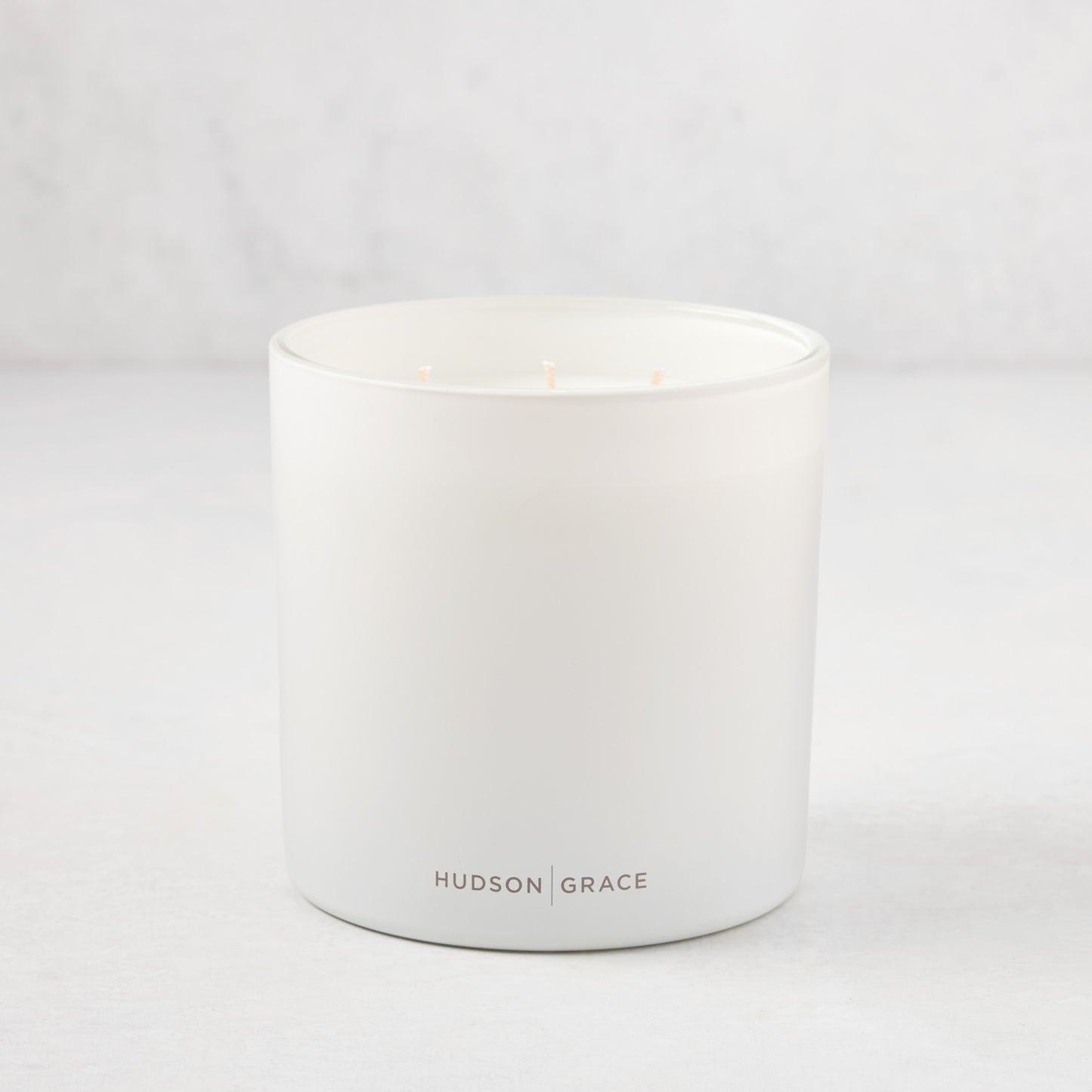 Hudson Grace Greenwich 3-wick candle in a white matte glass vessel with light pink wicks.
