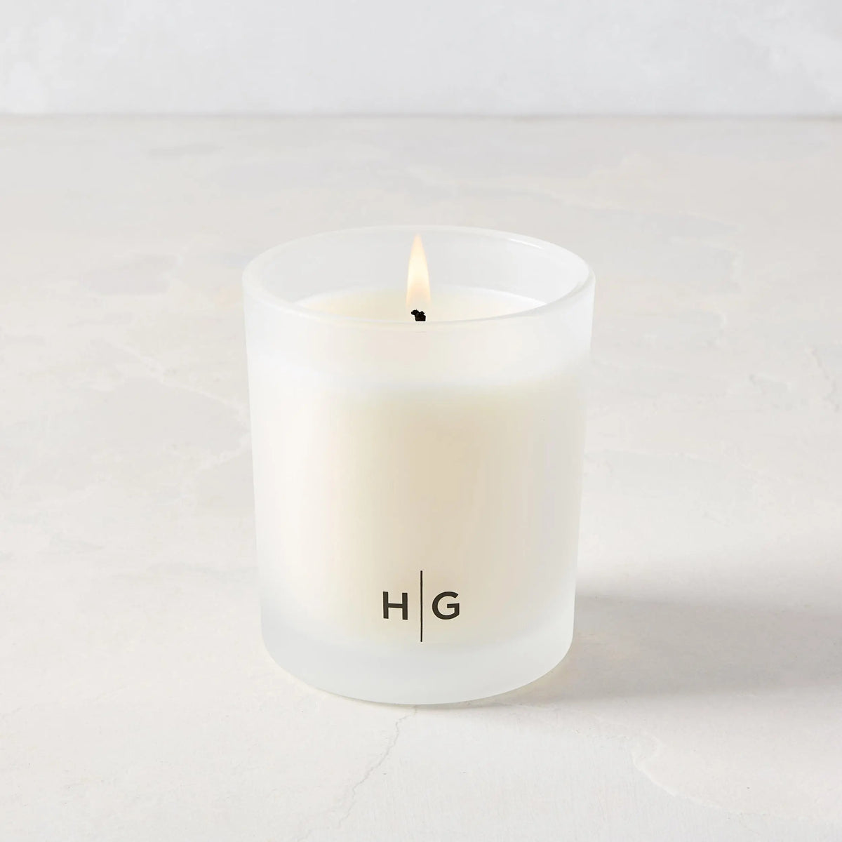 Hudson Grace San Marzano scented candle in a frosted glass vessel with "HG" logo, lit wick.