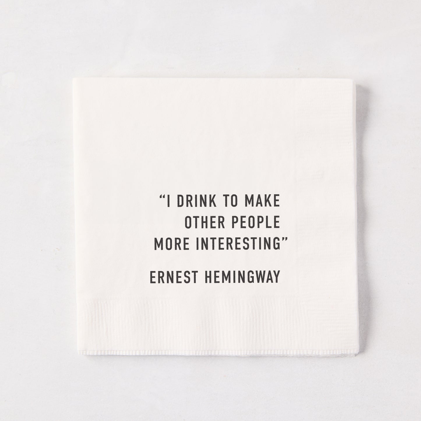 White 5.5-inch square 3-ply paper cocktail napkin with black text reading I Drink To Make Other People Interesting.