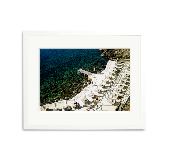 Il Pellicano Paradise framed wall art print of an Italian hotel's seaside terrace with lounge chairs and clear blue water.