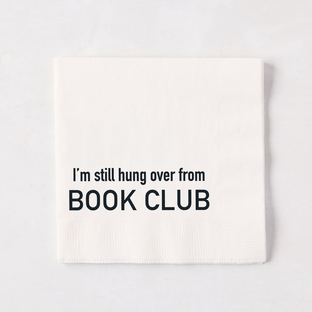White 5.5-inch square 3-ply paper cocktail napkin with black text reading I'm still hung over from BOOK CLUB.