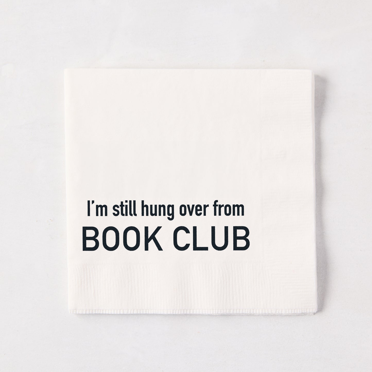 White 5.5-inch square 3-ply paper cocktail napkin with black text reading I'm still hung over from BOOK CLUB.