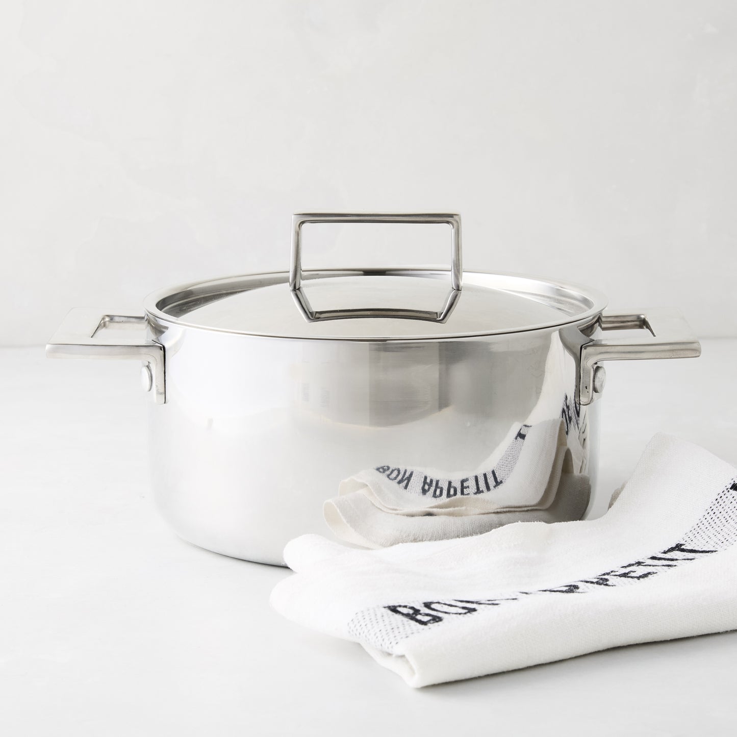 Italian 3-liter stainless steel casserole pot with lid and handles, beside a white "Bon Appetit" towel.