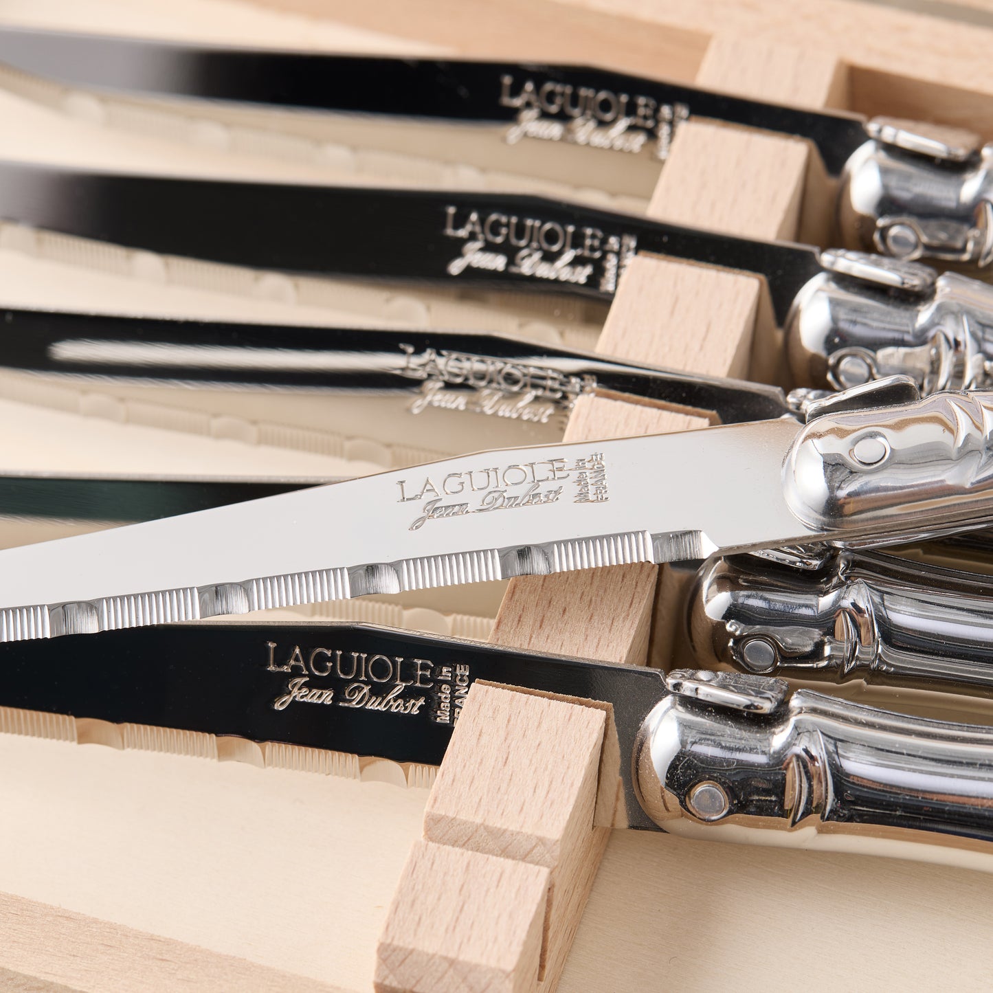 Jean Dubost Laguiole stainless steel table knives with serrated blades in a wooden storage box.