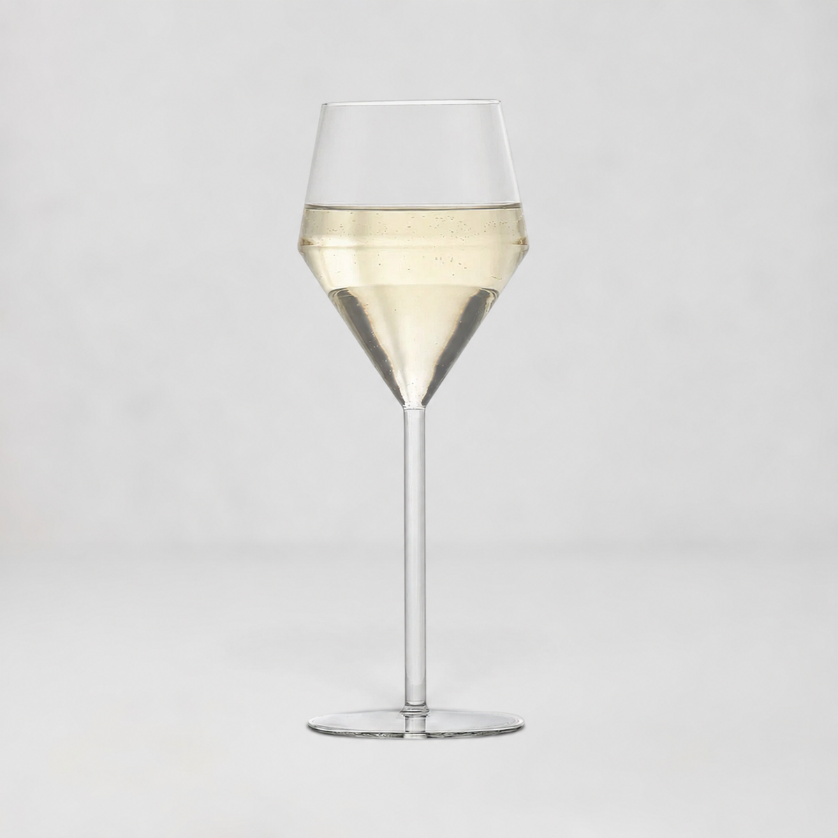 A clear glass wine glass with a wide bowl, a tapered middle section, and a long stem, shown on a light gray studio background. The glass is partially filled with a pale golden liquid.