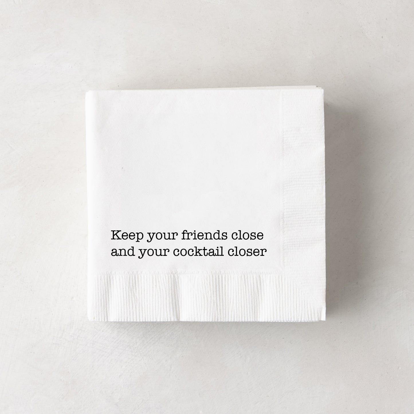White 3-ply paper cocktail napkins with "Keep your friends close and your cocktail closer" in black text.