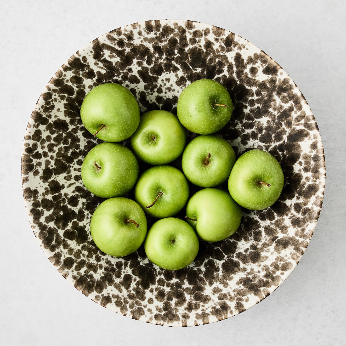 Large Nuno Splatter stoneware serve bowl with brown spots on cream, holding green apples.