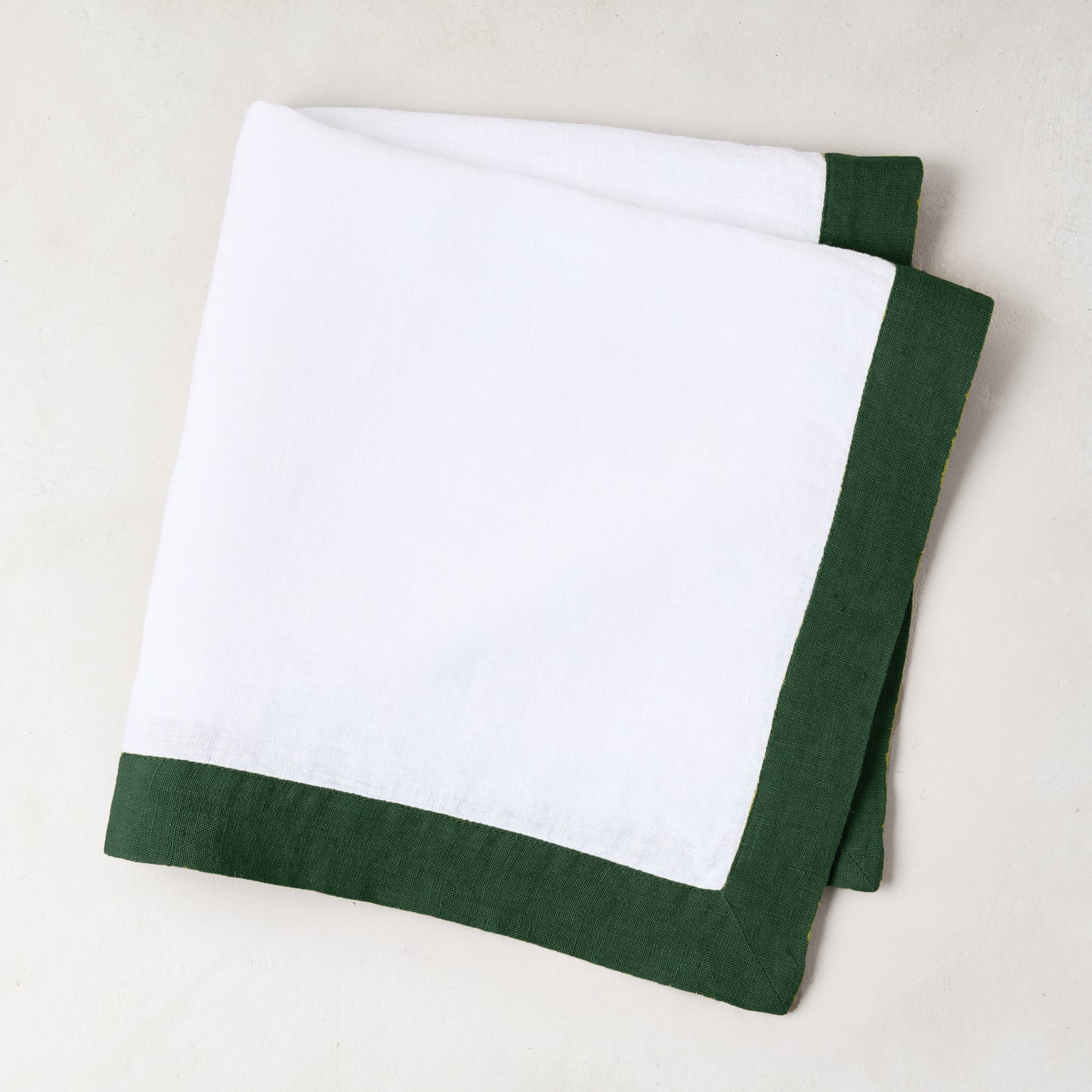 Folded white linen napkin with a fir green border.