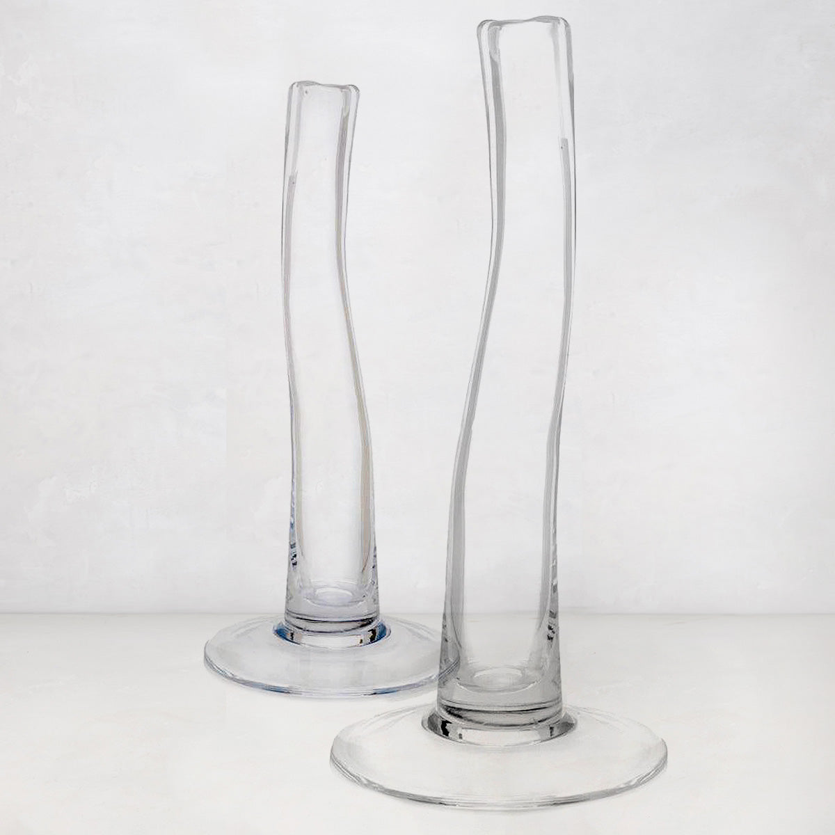 Two clear, tall, slender glass vases with scissor-cut mouths and wide bases.