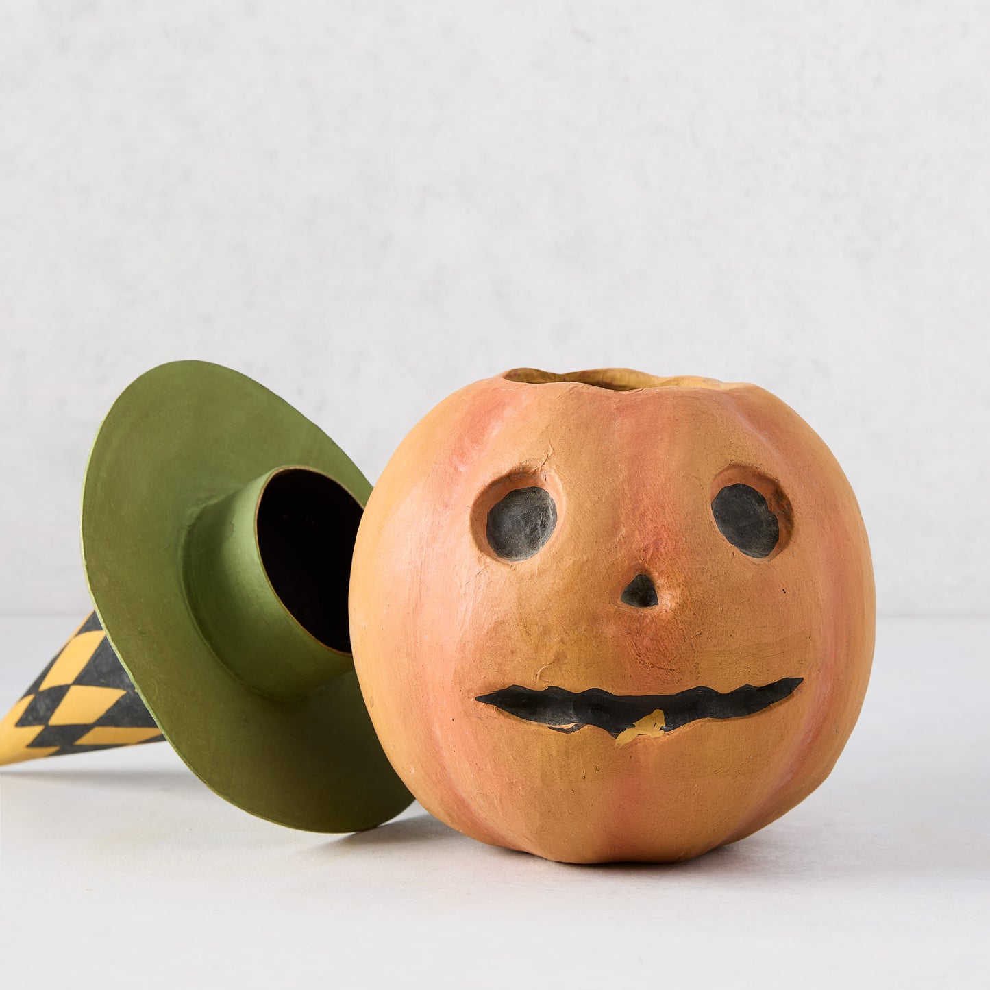 Vintage-style papier-mâché pumpkin candy bucket with a removable green and black checkered witch hat.