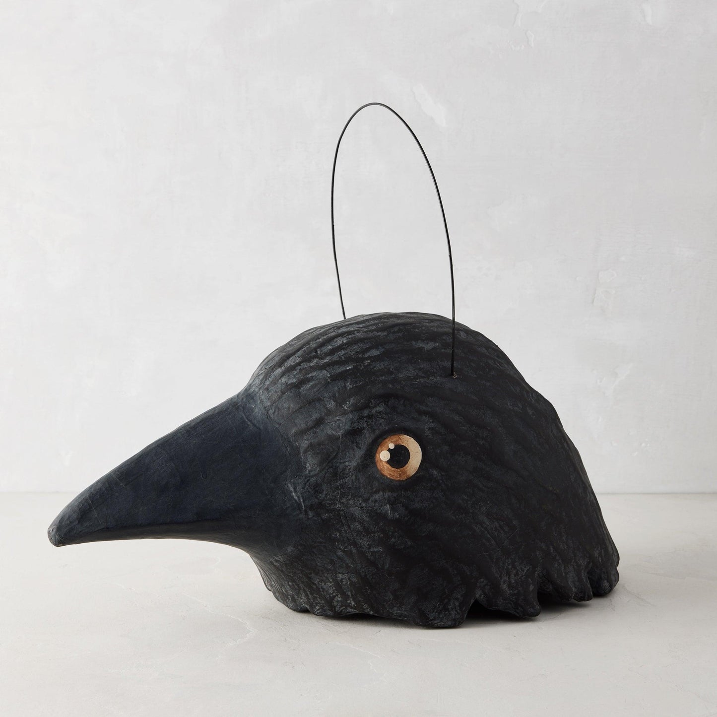 Black papier-mâché raven candy bucket with a distressed finish, wire handle, and vintage-style eye, 17 inches long.