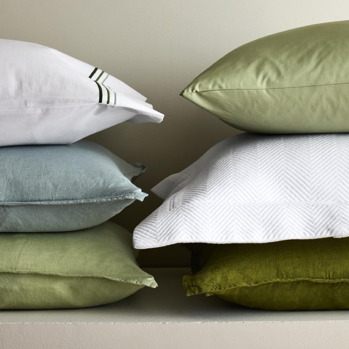 Stacked mint green, sage, and white linen and textured shams in various shades and weaves.