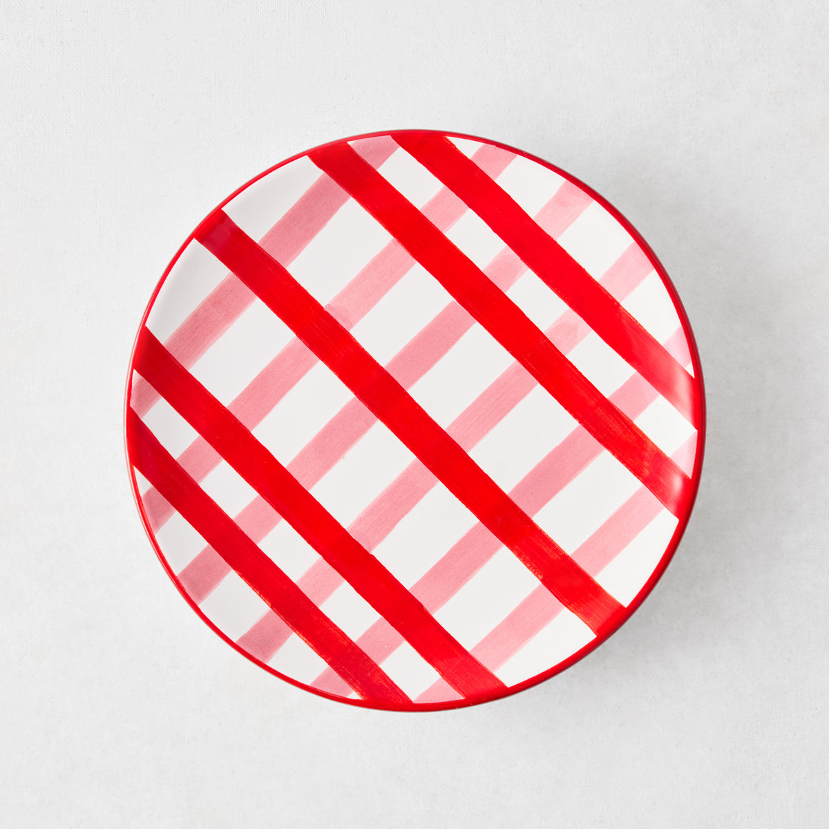 Round ceramic appetizer plate featuring a diagonal pink and red plaid pattern on a white background.