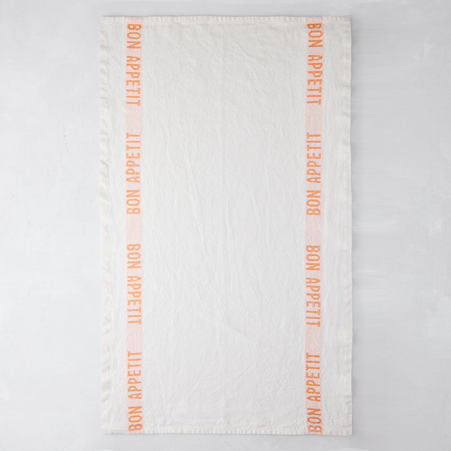 White linen hand towel with orange "Bon Appetit" text stripes.