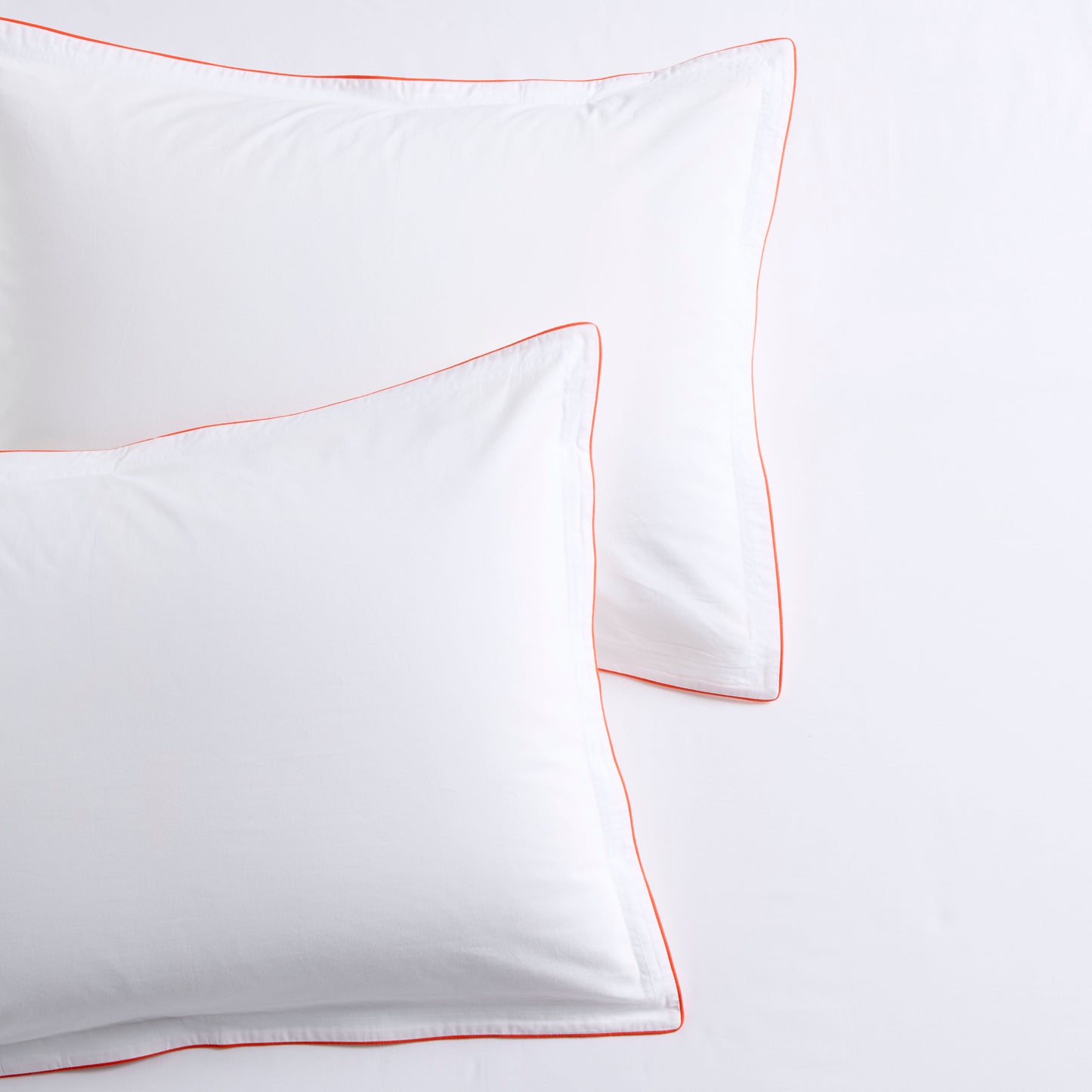 White percale pillow shams with orange piping and double-stitch detailing.