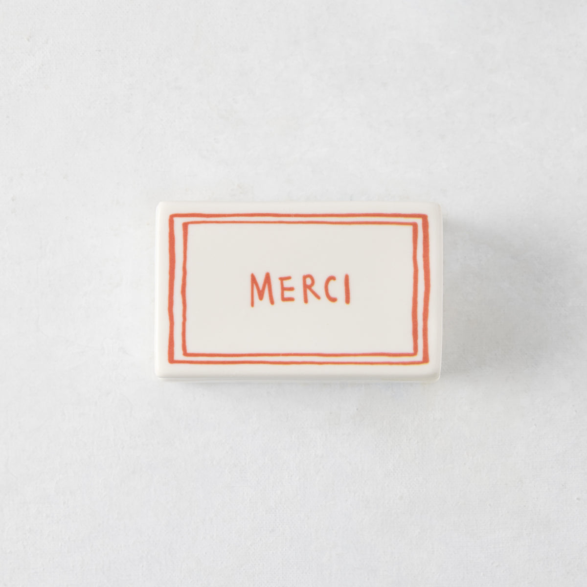 Rectangular white porcelain match box with red hand-painted border and Merci lettering, 3.54 x 2.17 inches.