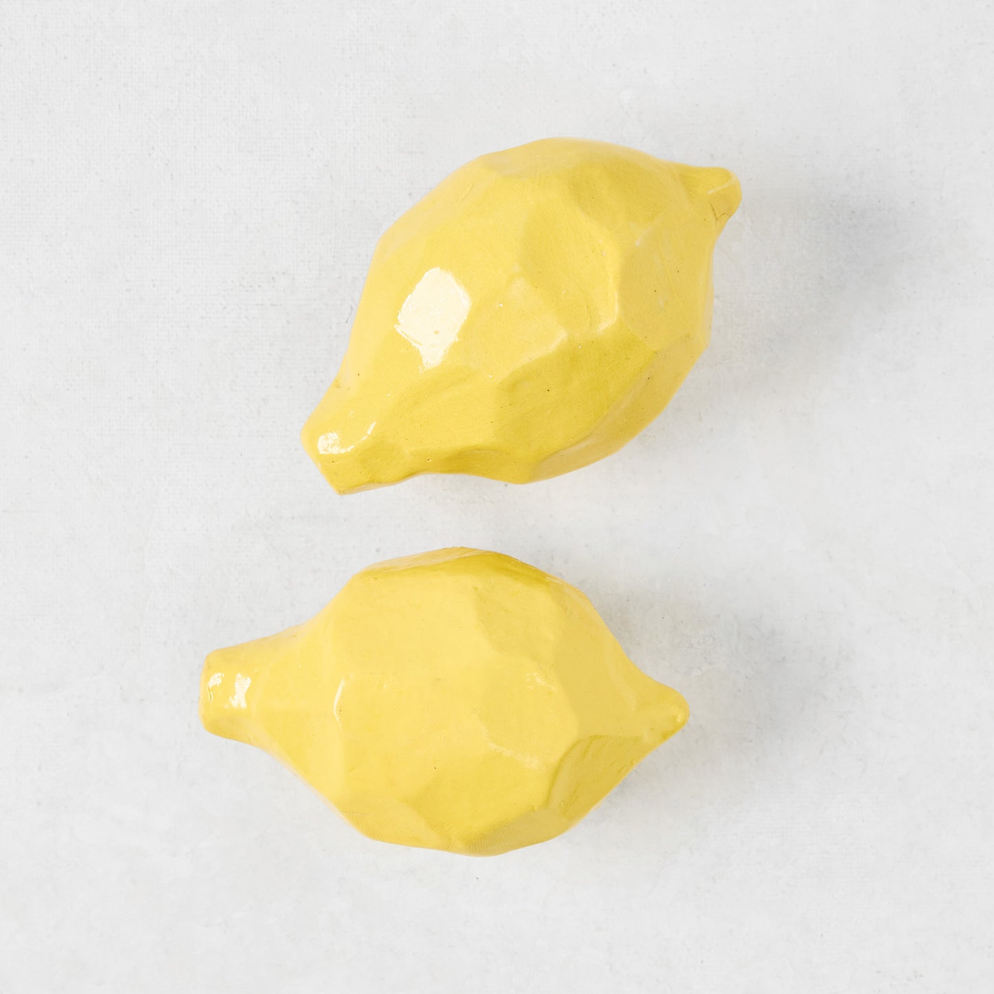 Two glazed yellow paper mache decorative lemons with faceted surfaces.
