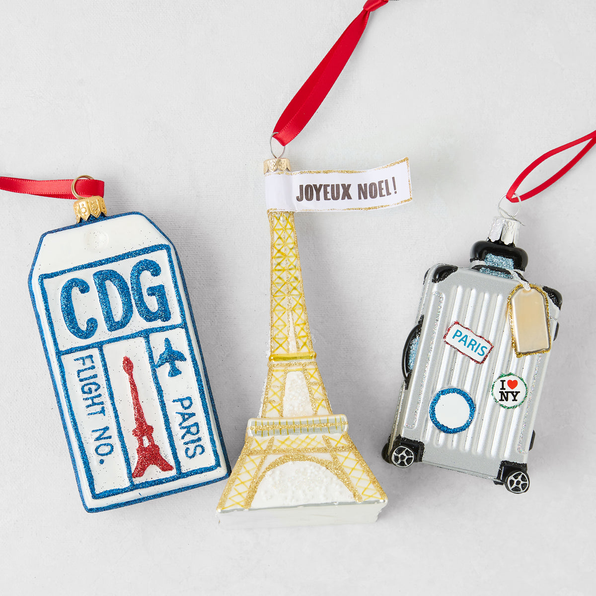 Parisian-themed Christmas ornament set featuring a glittery CDG luggage tag, gold Eiffel Tower, and silver suitcase.