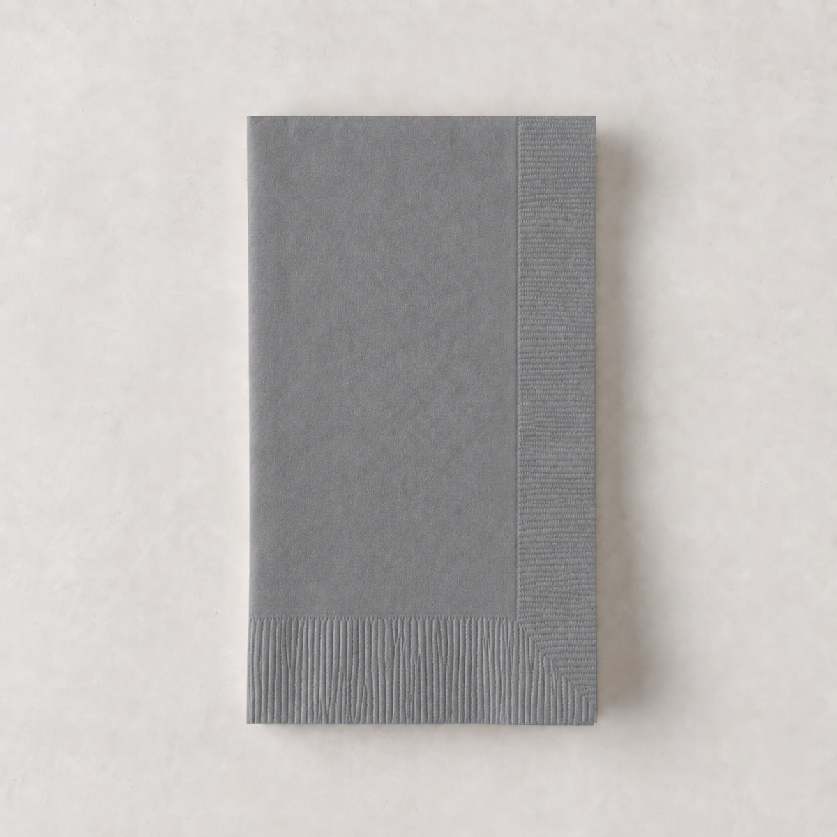 Folded grey 3-ply paper hand towel with a textured border on a light neutral background.